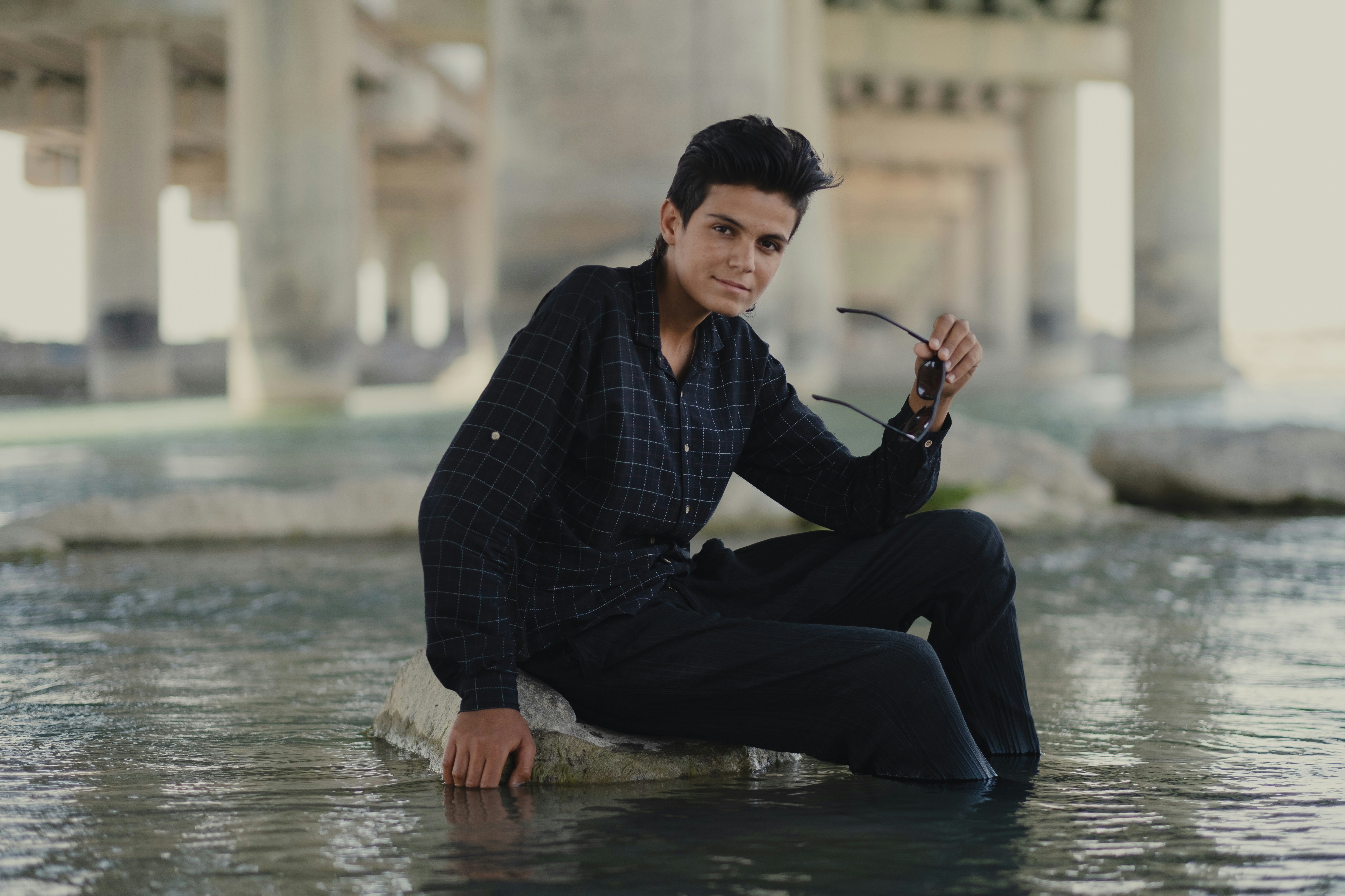 man in black and white checkered dress shirt and black pants sitting on water